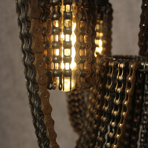Close-up van een kroonluchter gemaakt van metalen fietskettingen, met daarin verhelderende gloeilampen.