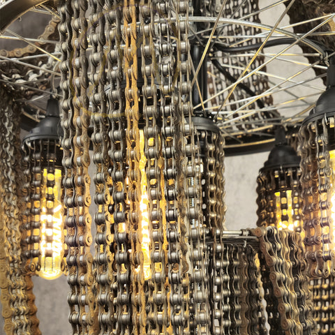 Een decoratieve lamp gemaakt van oude fietskettingen, met meerdere naar beneden hangende kettingstrengen, waarbij warme lichten de metalen schakels verlichten.